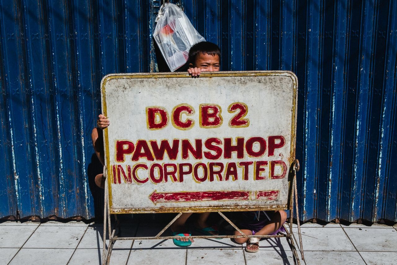 text, communication, western script, blue, one person, metal, corrugated iron, day, men, iron, real people, front view, architecture, sitting, container, lifestyles, leisure activity, young adult, sign, social issues