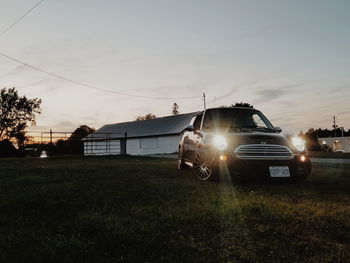 Cars on illuminated field against sky during sunset