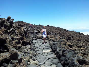 Rear view of woman walking on rocks against clear blue sky