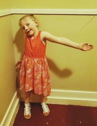 Portrait of smiling girl gesturing while standing against wall at home
