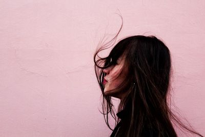 Close-up of young woman with tousled hair against wall