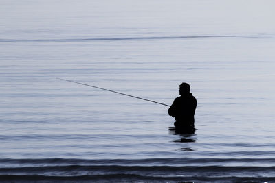 Silhouette man fishing in sea during sunset