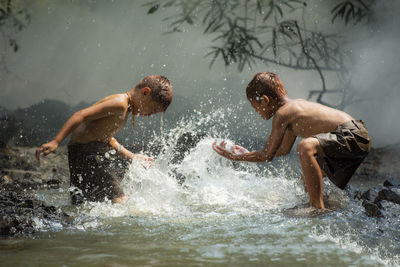 Side view of shirtless boys playing with water in river