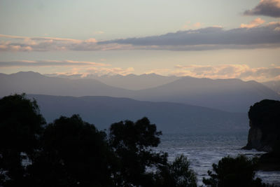 Silhouette trees by calm sea against mountain range