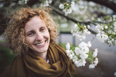 Portrait of smiling woman with curly hair by flowering tree