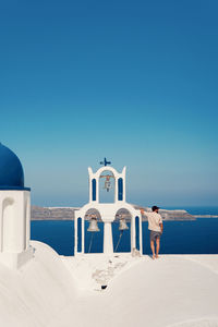 Lighthouse by sea against clear blue sky