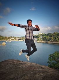 Full length of man jumping in lake against sky