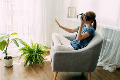 The girl is sitting in a chair with virtual glasses studying online or playing virtual games. 