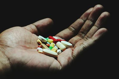Cropped hand of man holding medicines over black background