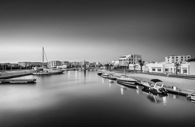 Sailboats moored in harbor by buildings against clear sky