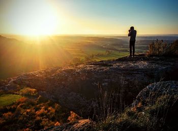 Man photographing while standing on rock during sunset