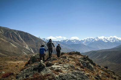 Rear view of people climbing mountain against clear blue sky