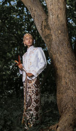 Man in traditional clothes standing by tree