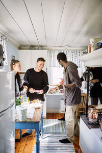 Happy friends talking while standing by food in kitchen at home