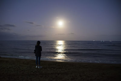 Rear view of woman standing on beach during sunset