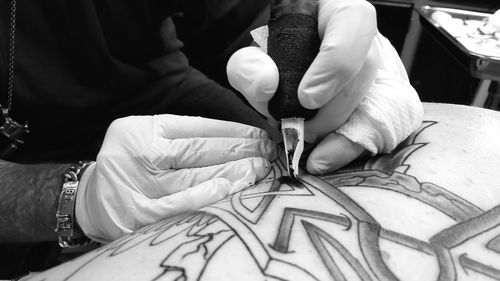 Cropped hands of artist making tattoo on person