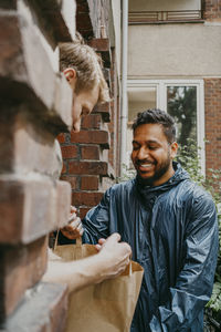 Smiling delivery person delivering parcel to man at doorstep