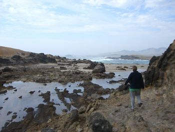 Rear view of woman standing on rock by sea against sky