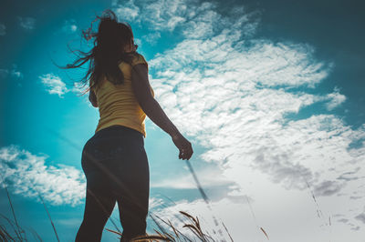 Low angle view of woman standing against cloudy sky