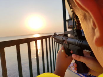 Midsection of person holding railing against sea during sunset