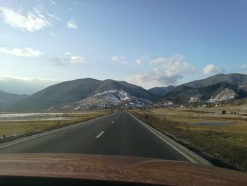 Road by mountains against sky seen through car windshield