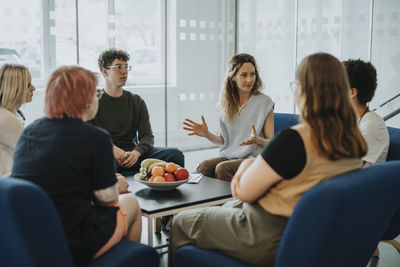 Mental health professional gesturing while guiding male and female students during group therapy