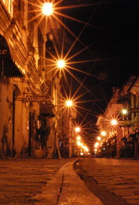 Illuminated street amidst buildings in city at night