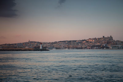 View of townscape by sea against clear sky at sunset
