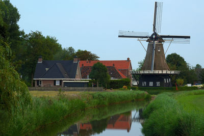 Traditional windmill by lake against sky
