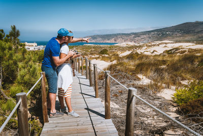 Side view of couple standing on footbridge against sky