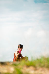 Side view of young woman using smart phone while sitting on mountain against sky