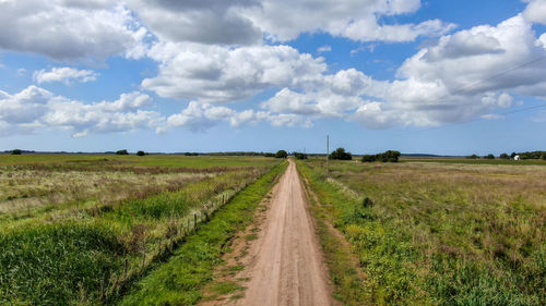 Dirt road amidst field against sky