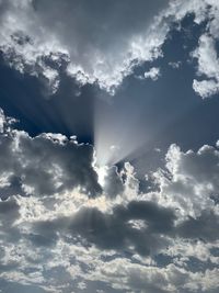 Low angle view of sunlight streaming through clouds