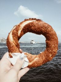 Woman holding pastry against boat in sea