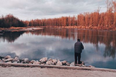 Rear view of man standing by lake against sky