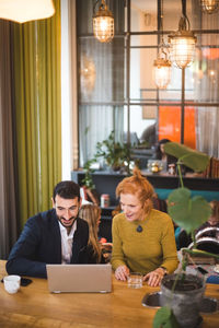 Smiling business colleagues discussing over laptop at table in office