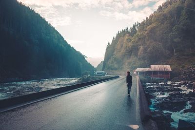 Woman walking on road amidst mountains against sky