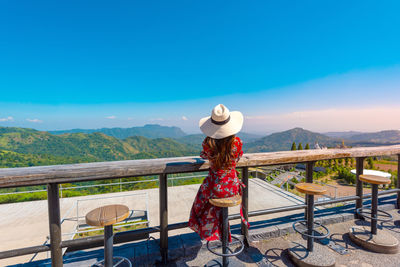 Woman standing on railing against mountain and blue sky