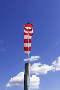 A windsock on flagpole against blue cloudy sky white and red striped conical textile tube