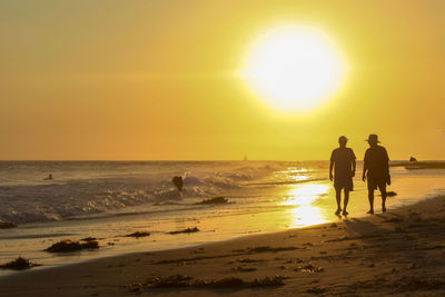 Rear view of woman walking at beach against sky during sunset