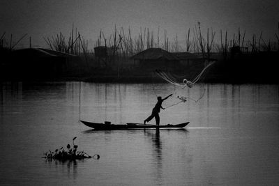 Silhouette man throwing fishing net in river at dusk