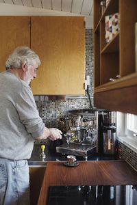 Senior man using coffee maker on kitchen counter at home