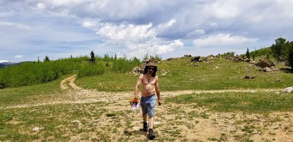 Shirtless man walking on field against sky