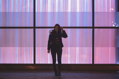 Woman standing against illuminated wall at night