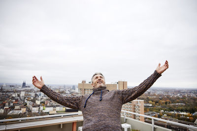 Man standing with arms outstretched against cityscape in background