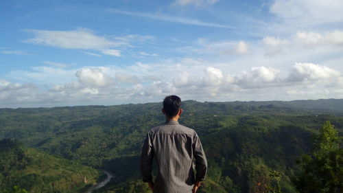 Rear view of man standing on mountain against sky