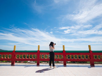 Rear view of woman standing on railing against sky