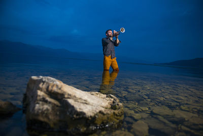 Man standing on rock by sea against sky