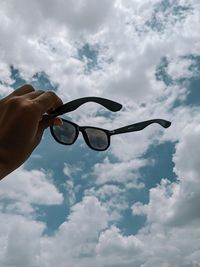 Low angle view of hand holding sunglasses against sky