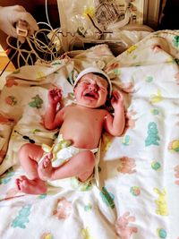 High angle view of newborn baby with umbilical cord crying on bed at hospital